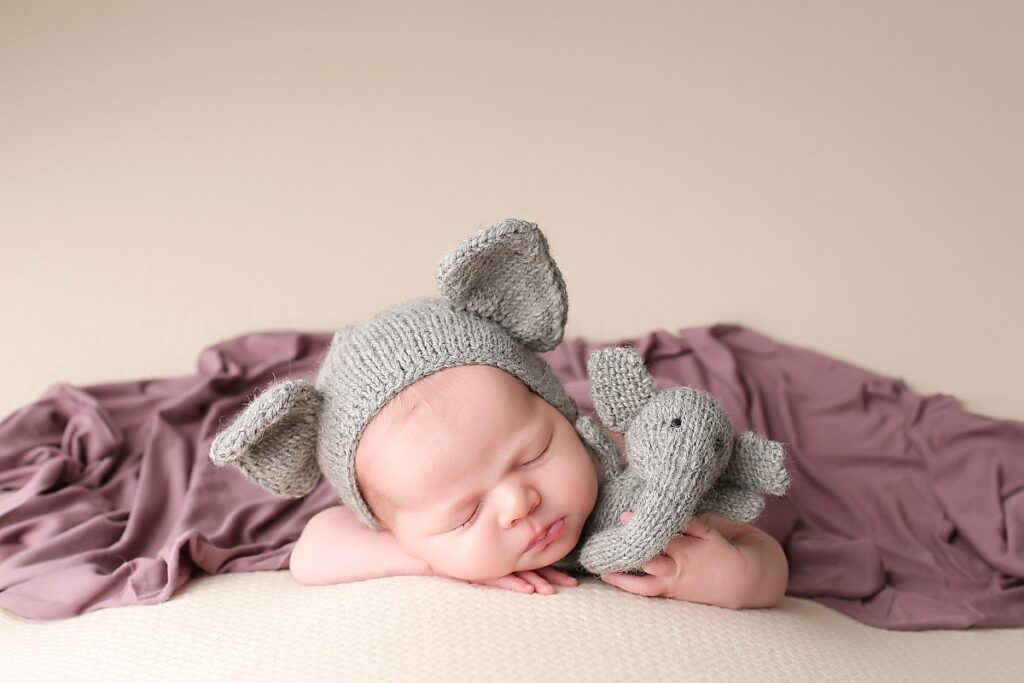 Baby girl sleeping in a bonnet with elephant ears, holding a stuffed elephant