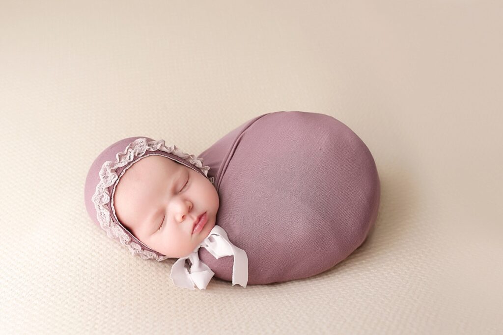Baby girl sleeping swaddled in a purple wrap and matching bonnet
