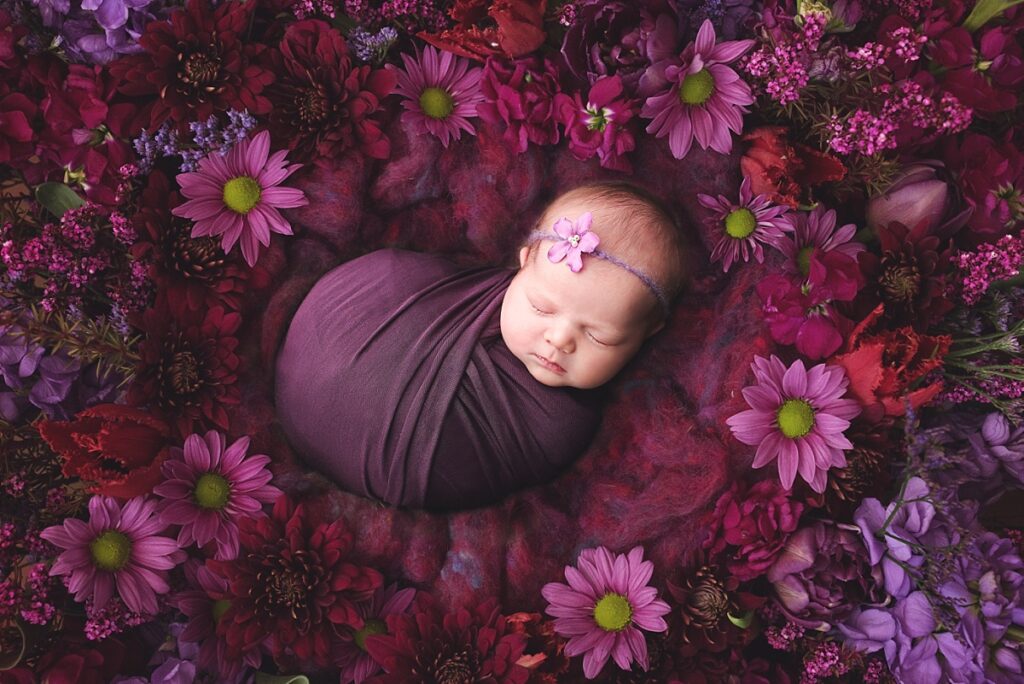 Baby girl sleeping on a bed of purple flowers