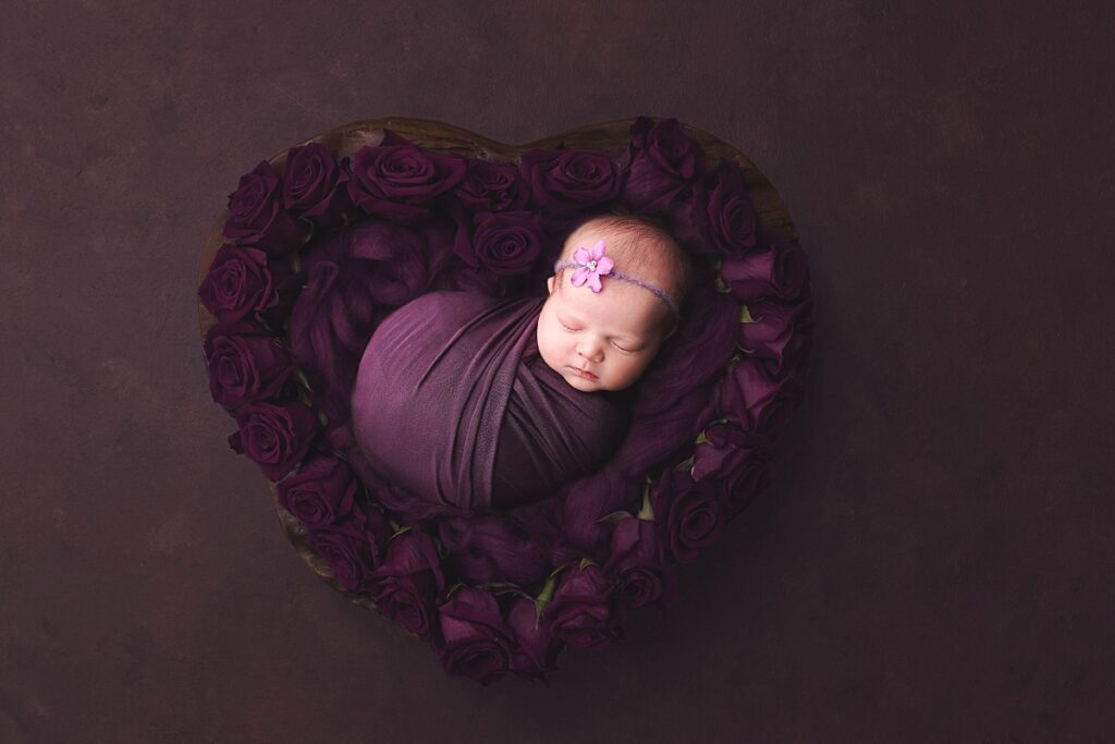 Baby girl wrapped in purple lying in a heart shaped bowl