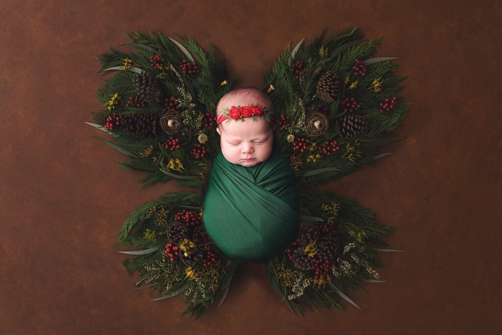 Baby girl wrapped in green and red on a bed of holiday garland