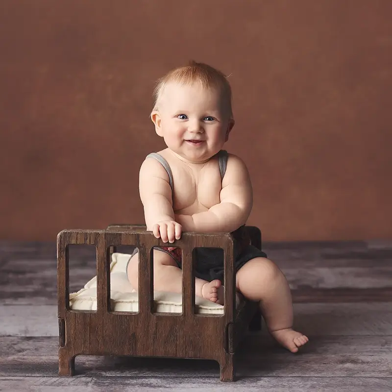KC-baby-boy-sitter-portrait-session Chubby baby boy sitter photo sitting in a small wooden bed prop with rust orange background during milestone session