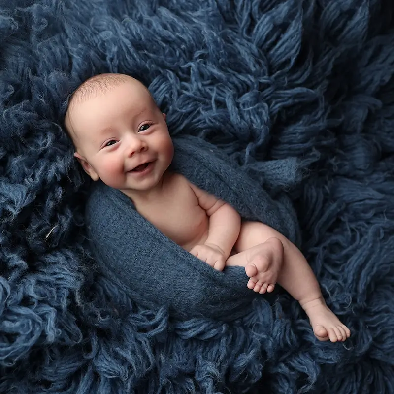 Kansas-City-baby-photography-studio-session-boy-smiling-wrapped-in-blue-knit-blanket Baby boy laughing and smiling wrapped in a blue knit and snuggled on a blue fur rug during his Kansas City Baby photography session