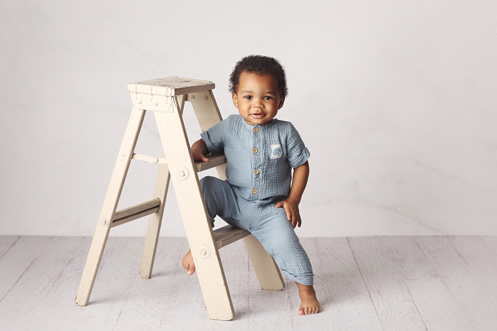 Baby boy posing on small ladder during milestone first birthday photography in Kansas City