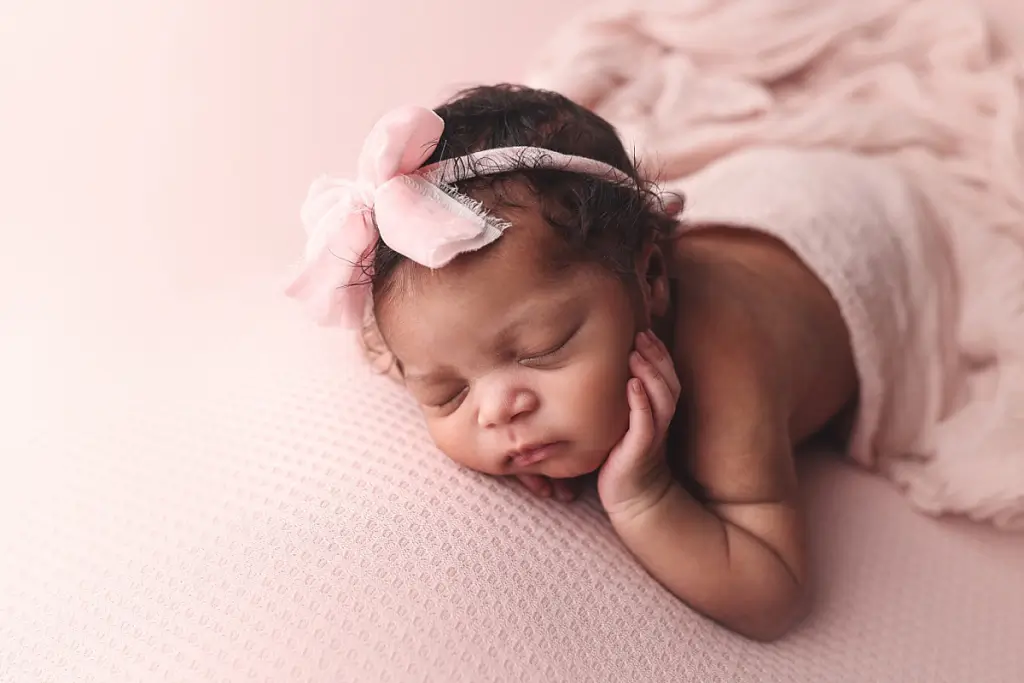 Close-up portrait of newborn girl peacefully sleeping in soft pink swaddle