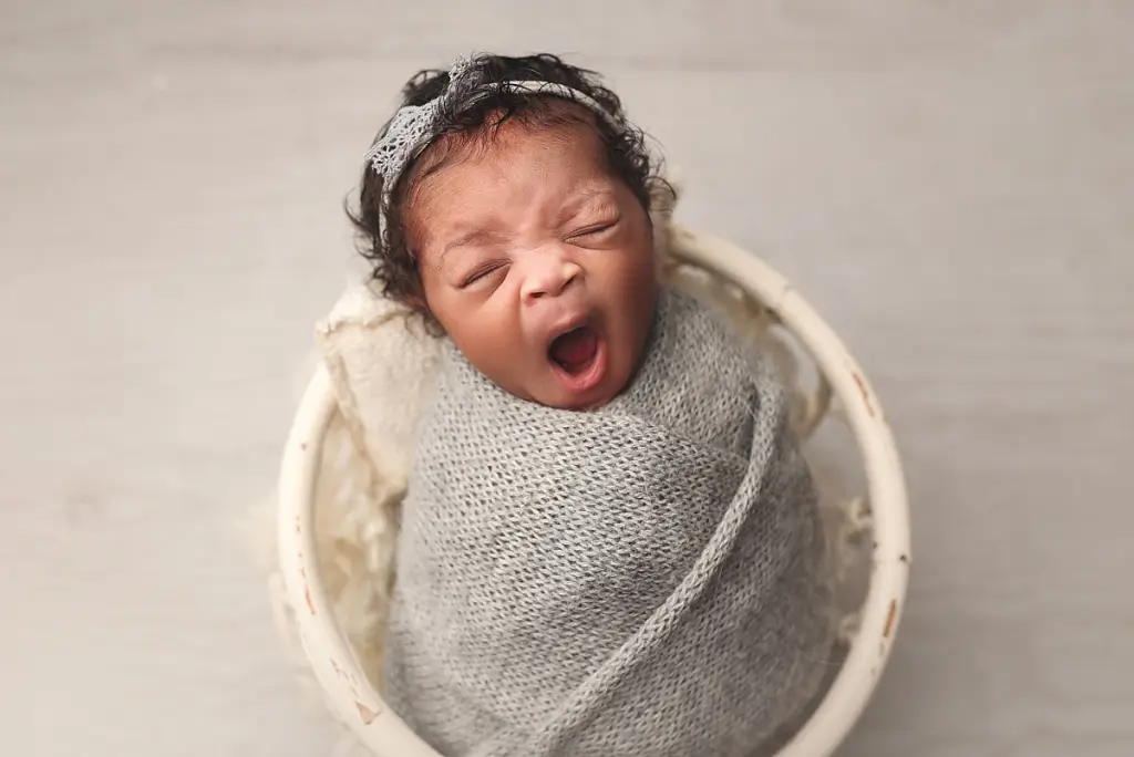 Newborn baby girl swaddled in soft grey wrap during cozy Kansas City newborn photography session