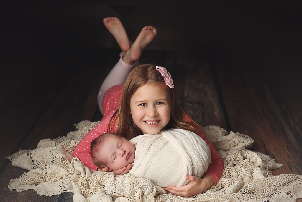 Smiling sister with swaddled newborn baby brother in cozy newborn portraits