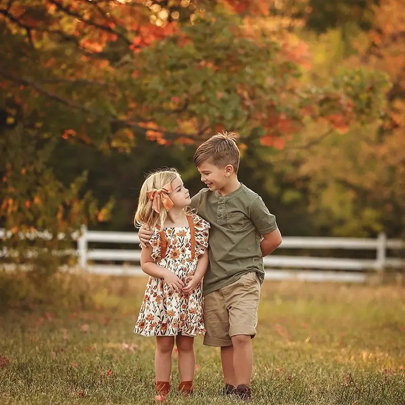 brother-and-sister-posing-with-fall-leaves-kansas-city-family-photos Brother and sister smile at each other with fall colors behind them at their outdoor Kansas City Family session