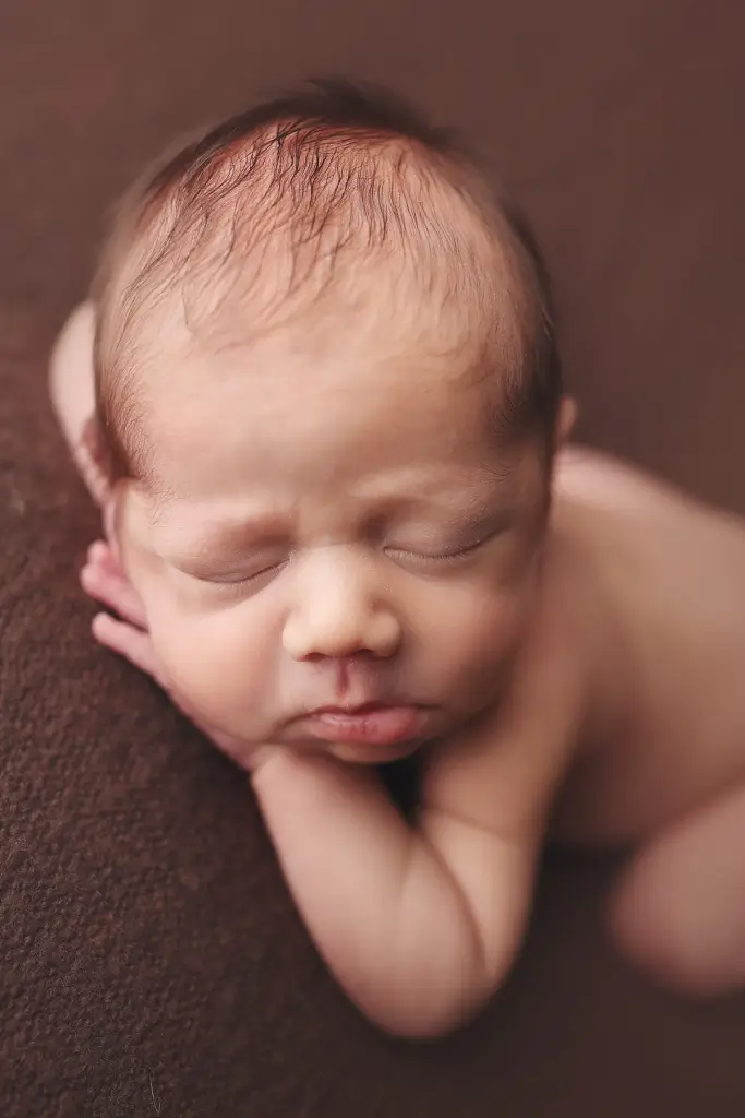 Professional newborn portrait of baby boy posed on brown fabric background in Kansas City studio
