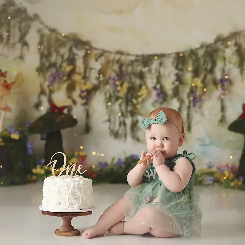 kansas-city-cake-smash-studio-session Baby girl woodland fairy themed cake smash with floral backdrop, mushroom props, green bow outfit, and white birthday cake