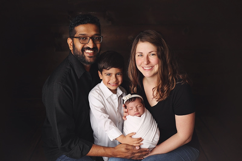 kansas-city-newborn-family-photo Family newborn portrait in Kansas City studio with parents and older sibling smiling while holding swaddled baby