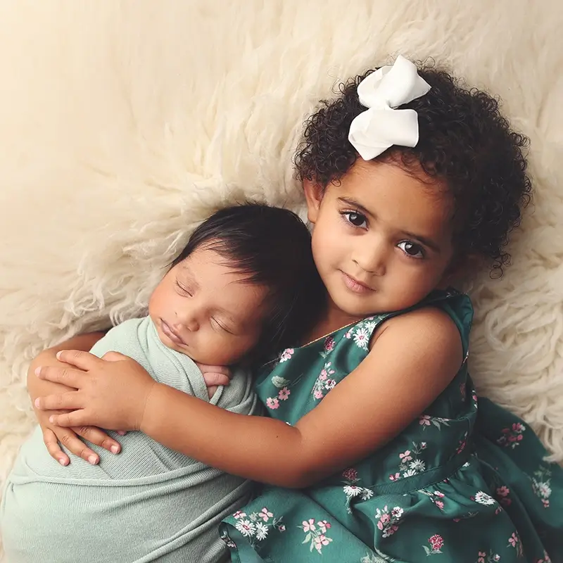 kansas-city-newborn-studio-session-siblings-snuggled-together Older sister snuggles her newborn brother at his newborn studio photography session in Kansas City