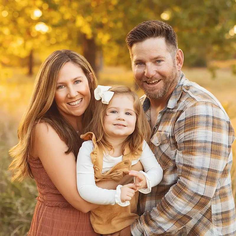 kansas-city-outdoor-family-fall-session-golden-hour Mom and dad hug their toddler age daughter at their Kansas City fall outdoor family session