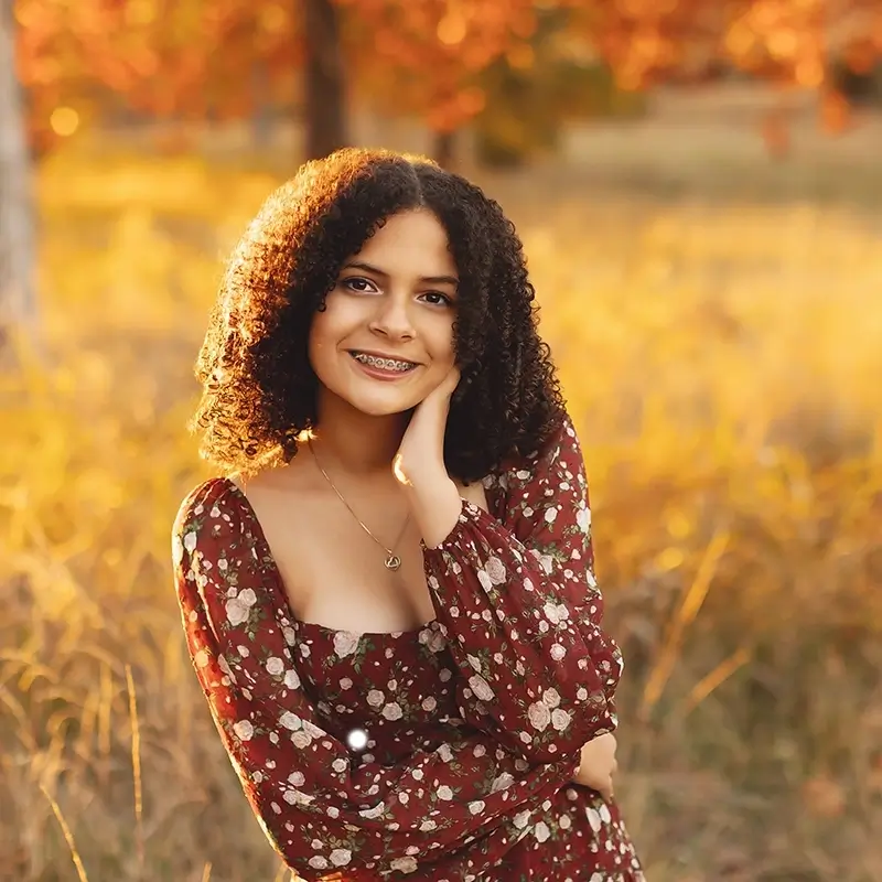 kansas-city-outdoor-family-portrait-fall-session Teen girl fall portrait in burgundy floral dress with curly hair, smiling in golden autumn sunset field in Kanas City