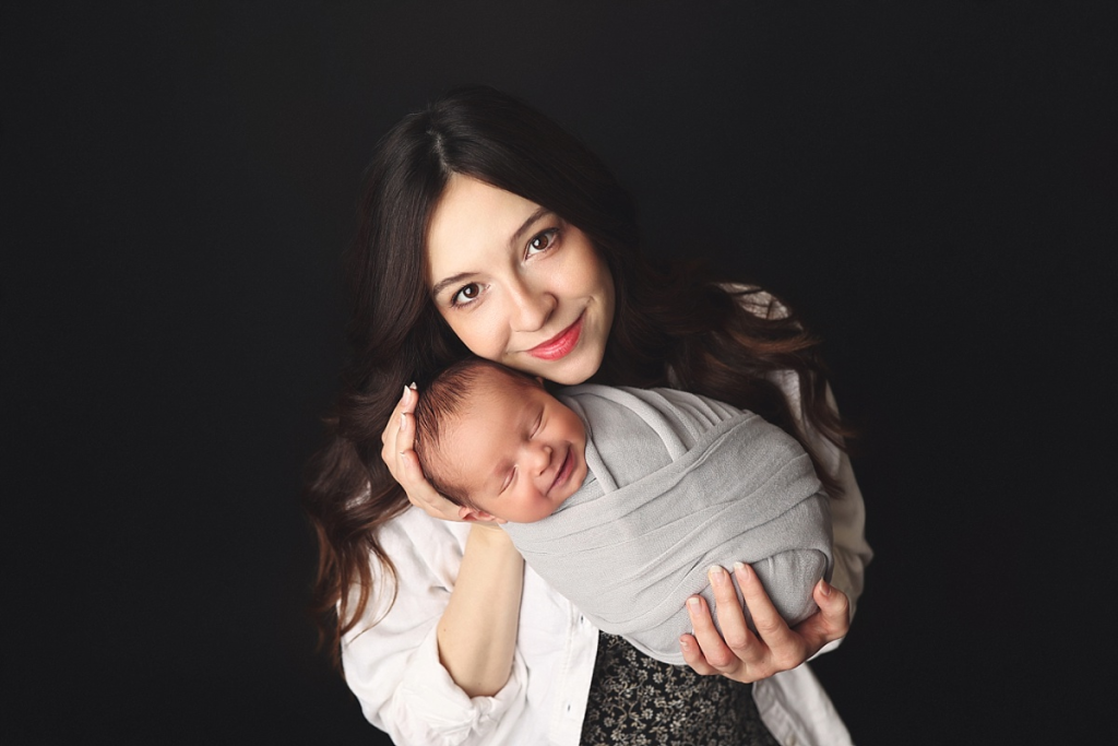 Mother cradling newborn son wrapped in soft blanket in Kansas City newborn studio
