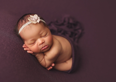 A newborn girl snuggles under a deep purple wrap while she sleeps soundly during her KC studio newborn session.