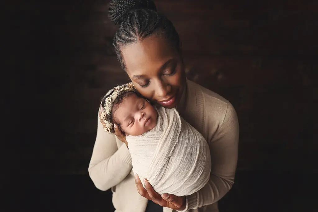 Tender portrait of mom cuddling baby girl in cozy Kansas City newborn studio
