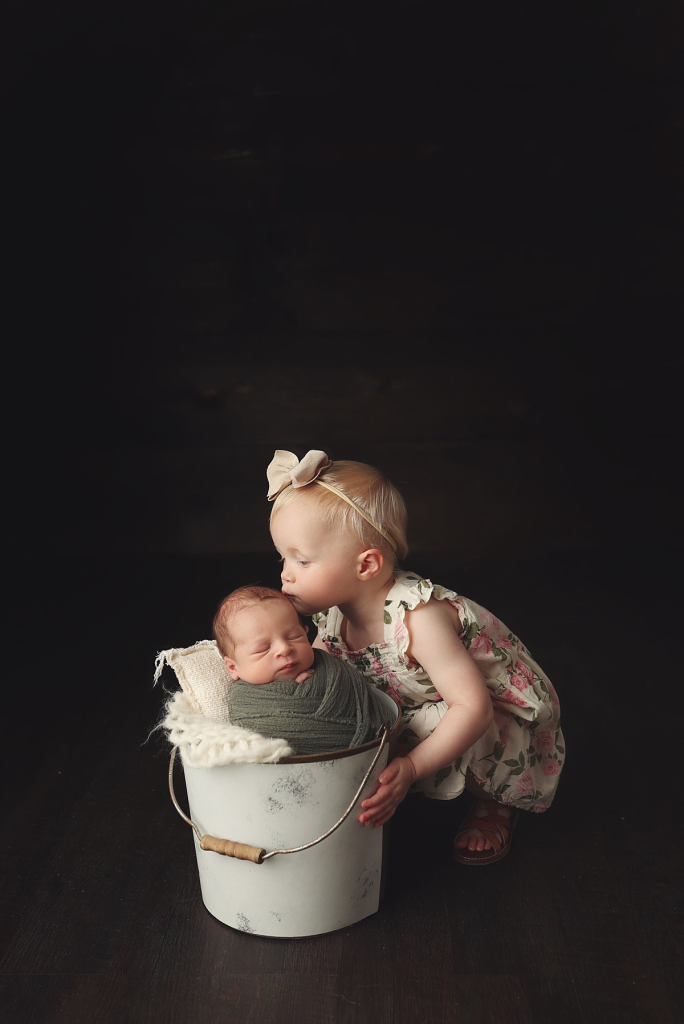 Sweet moment of sister giving newborn brother a kiss at Anna Marie Photography studio