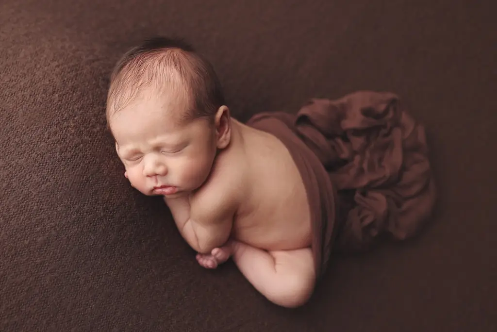 Sleeping newborn boy wrapped in chocolate brown swaddle in cozy Kansas City newborn studio