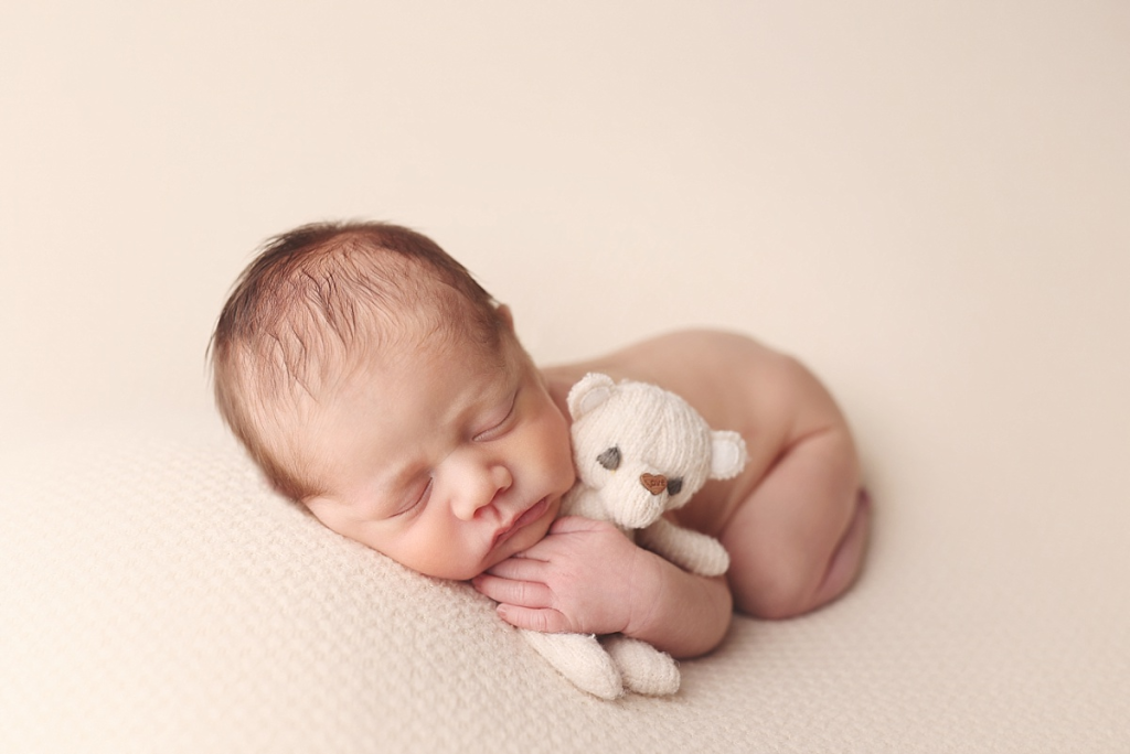 Newborn baby boy cuddling small teddy bear during cozy newborn portraits in Kansas City