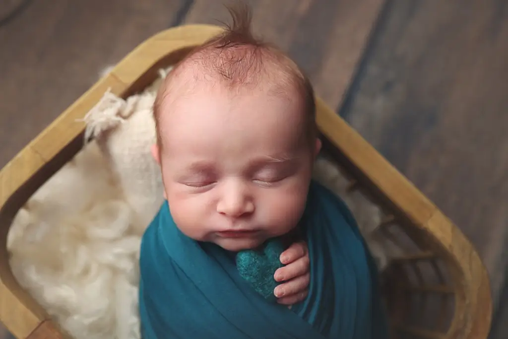 Newborn baby boy in wooden crate holding tiny felt heart at Anna Marie Photography studio