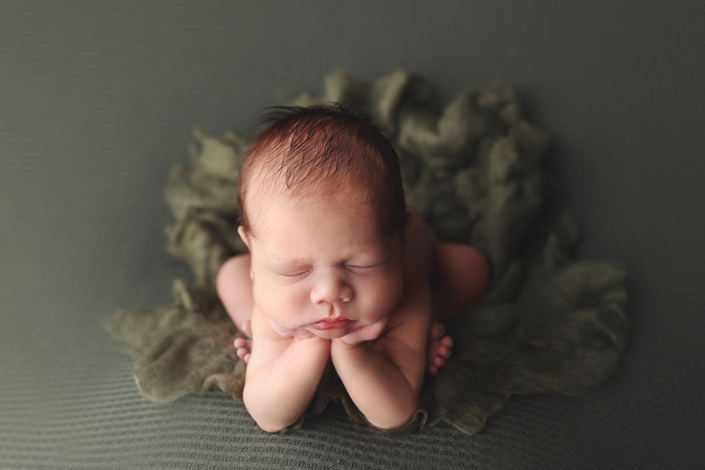 Newborn boy posed and sleeping on green fabric in Kansas City newborn photo studio
