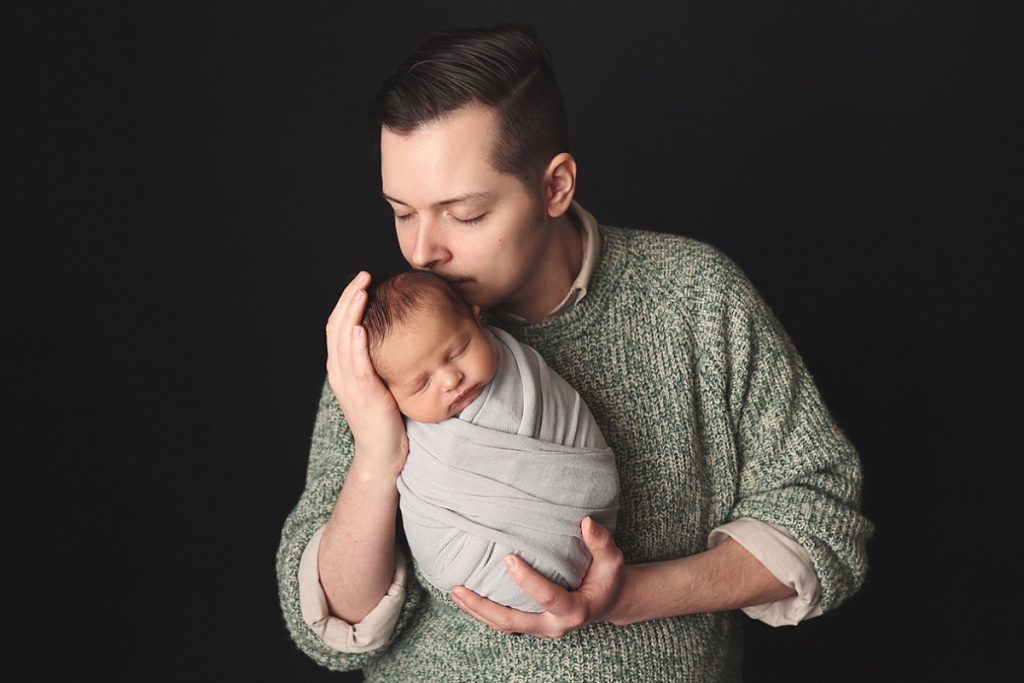 Father gently holding newborn baby boy during professional newborn photo session in Kansas City