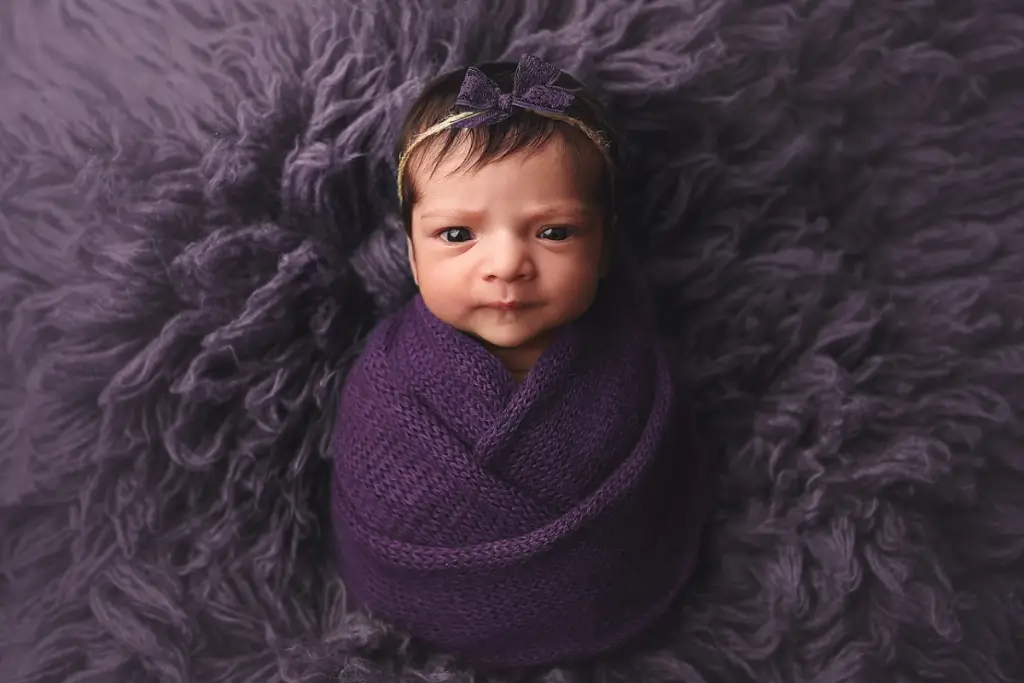 baby girl with open eyes looks at camera swaddled in purple at her Kansas City Newborn photoshoot