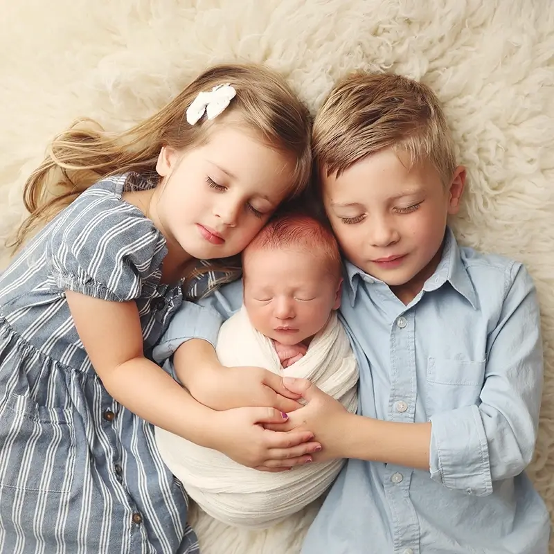 older-siblings-snuggling-their-newborn-brother-kc-newborn-session Big brother and sister cuddling newborn baby during studio portrait session testimonial from Megan
