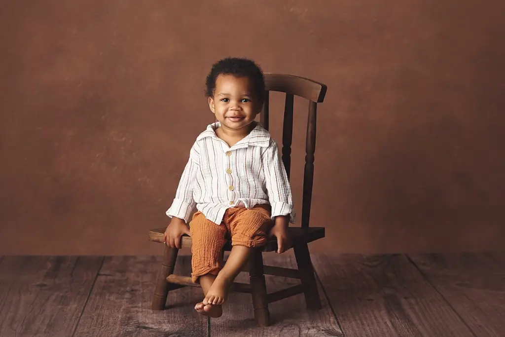 Baby boy sitting in tiny chair during first birthday portraits in Kansas City