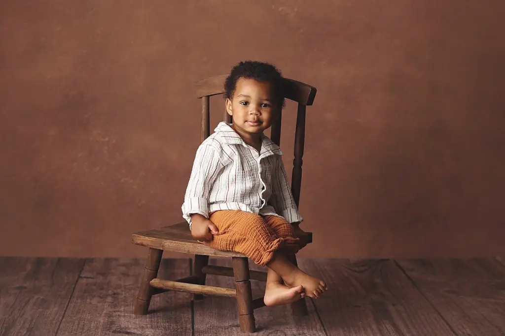 Smiling baby boy in wooden chair before cake smash session
