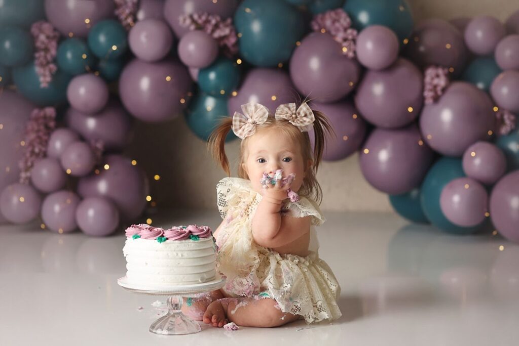 baby girl at cake smash in kansas city with purple and blue balloon garland