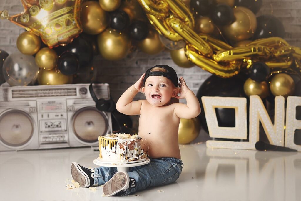 notorious one themed cake smash for little boy wearing jeans and cap at kansas city photography studio