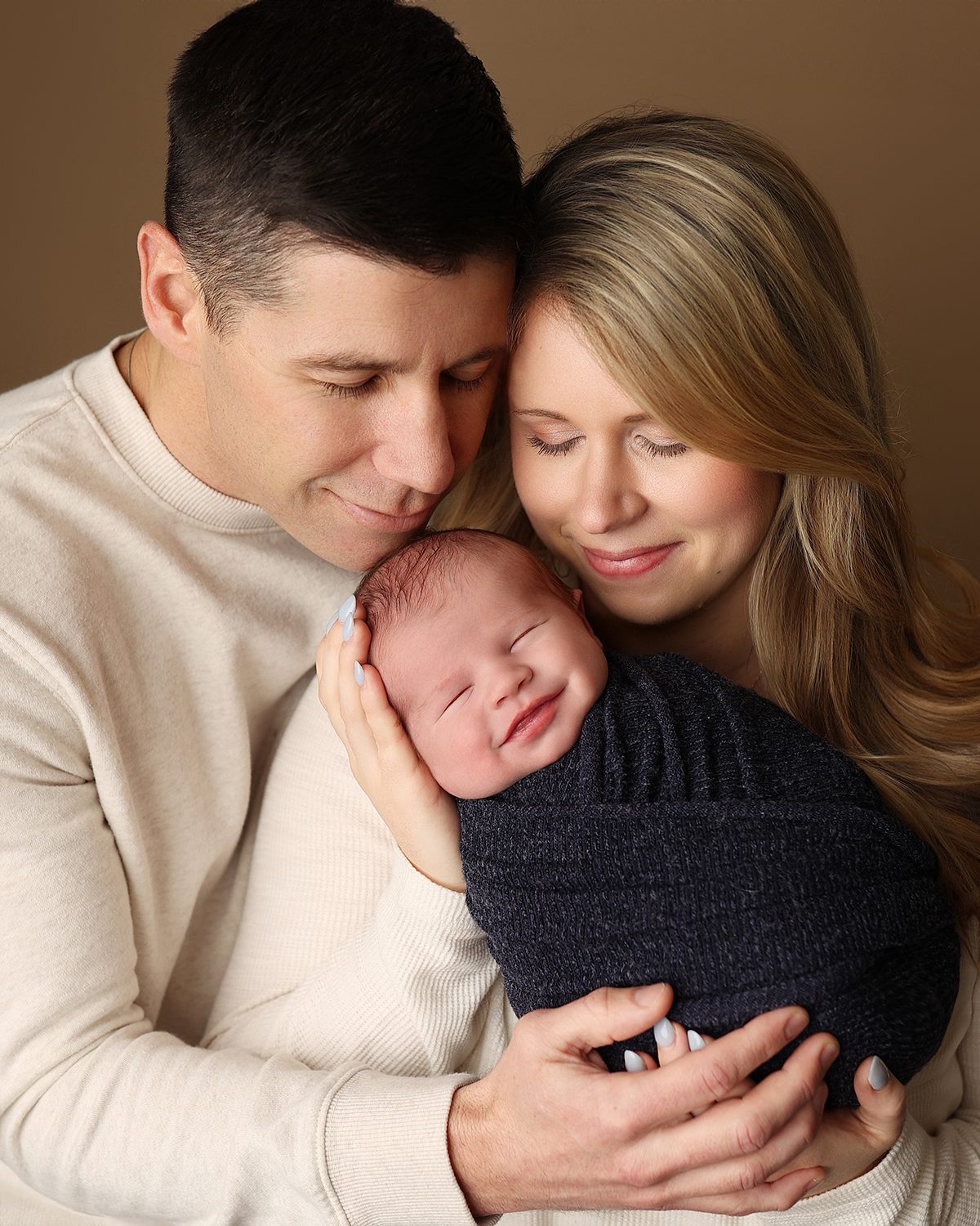 Parents cuddling their swaddled newborn baby during an in studio newborn photography session, capturing a quiet family moment