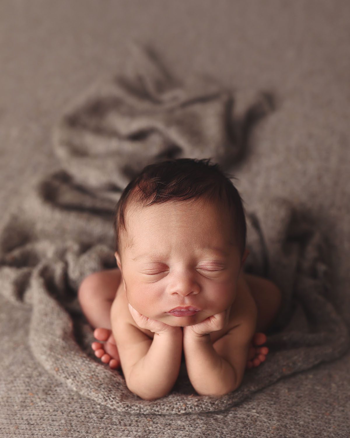 Sleeping newborn baby boy posed in the froggy position on a textured taupe blanket in a professional newborn photography studio