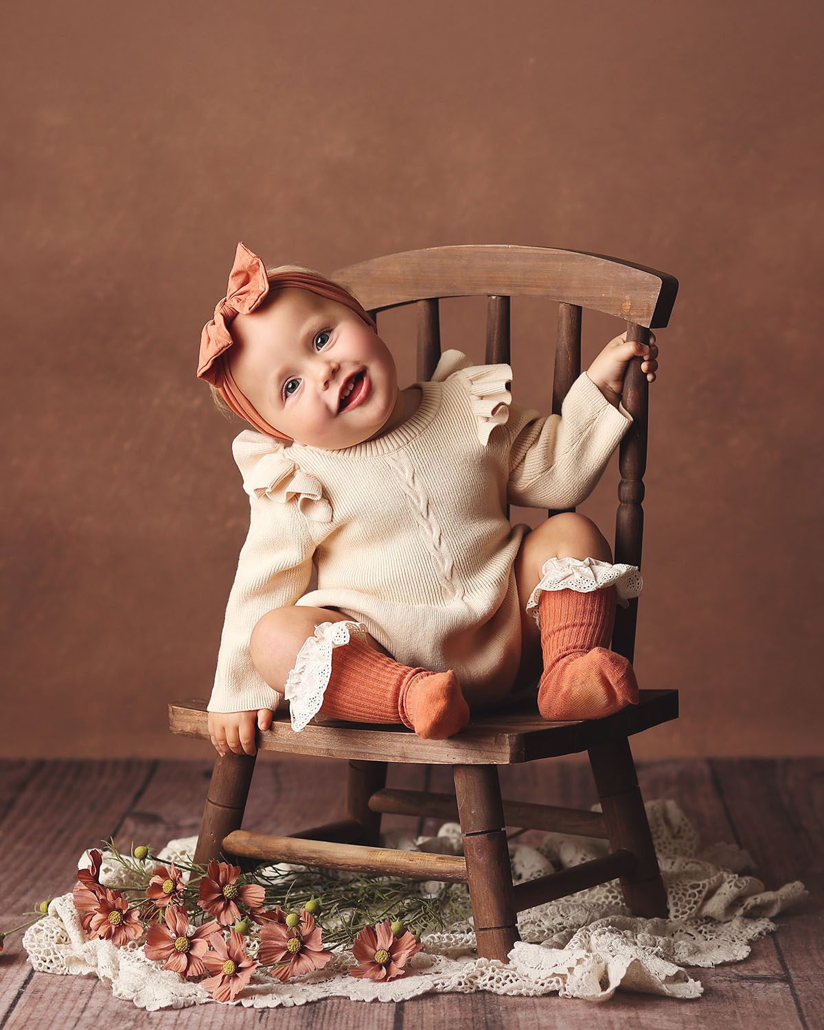 One year old girl milestone portrait sitting on a wooden chair wearing a sweater romper and rust colored knee socks.