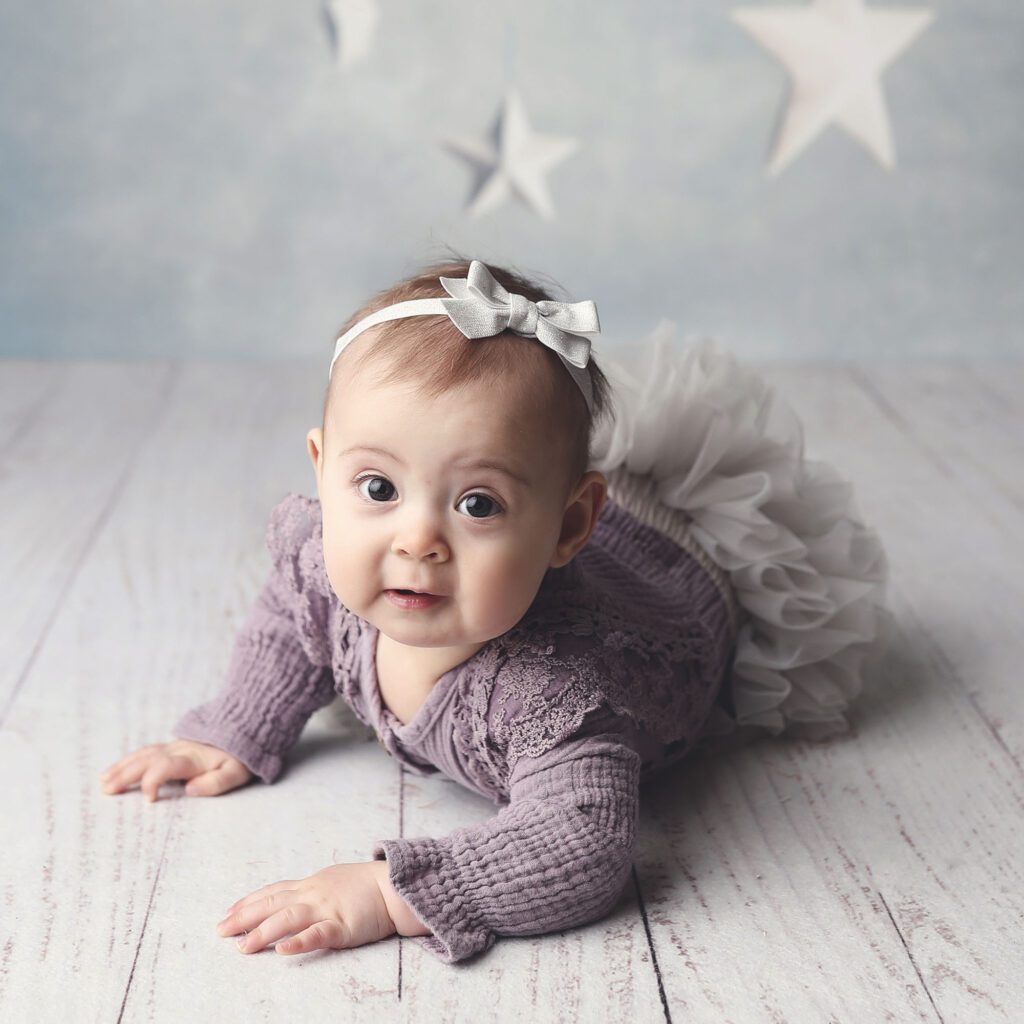 Baby girl in a purple dress lying on her tummy with a blue star backdrop