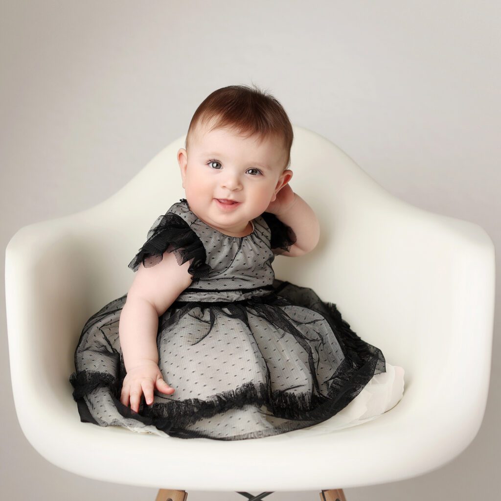 baby girl wearing a black tulle dress sititing in a white chair on a white backdrop