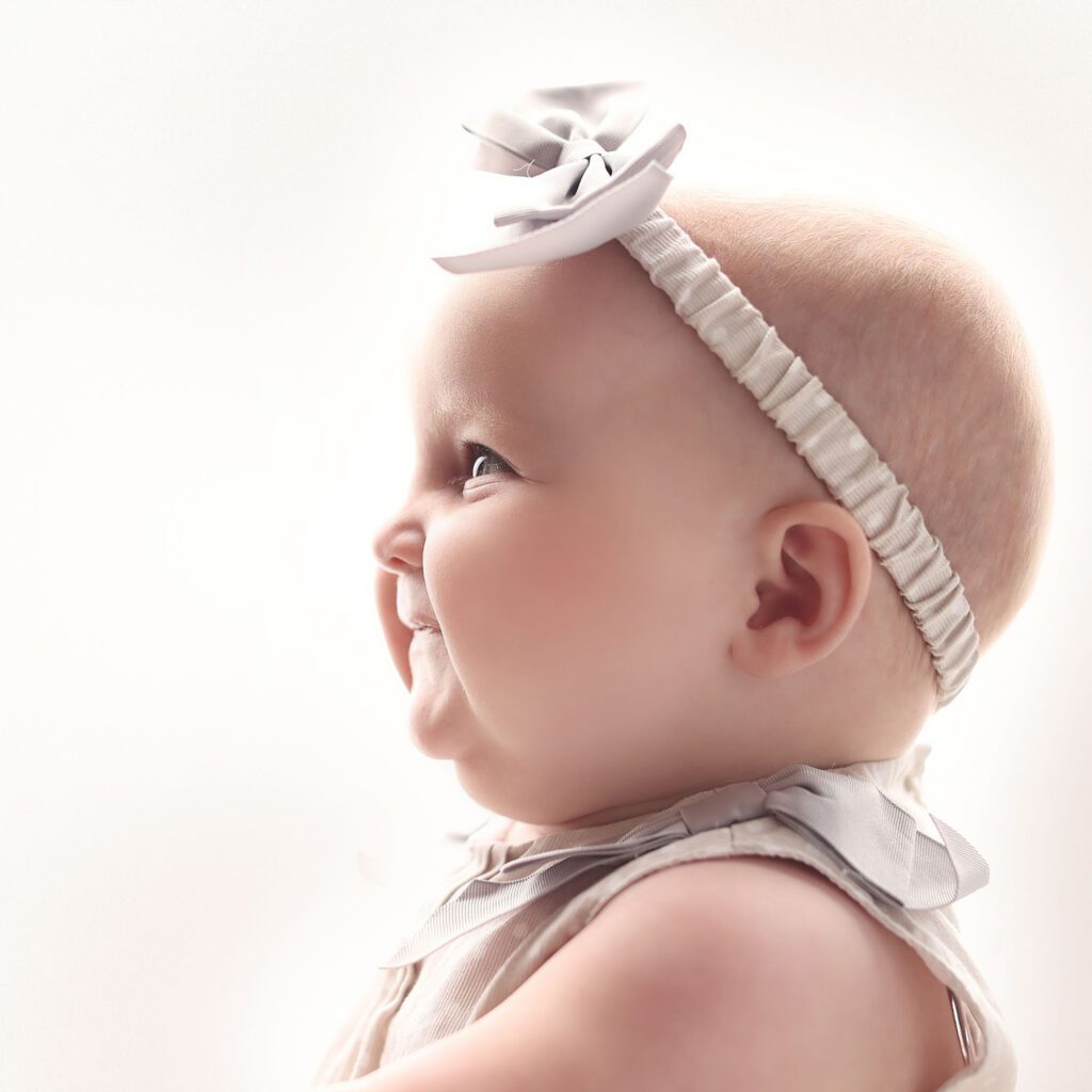 Backlit profile portrait of a smiling baby girl wearing a bow and looking upward