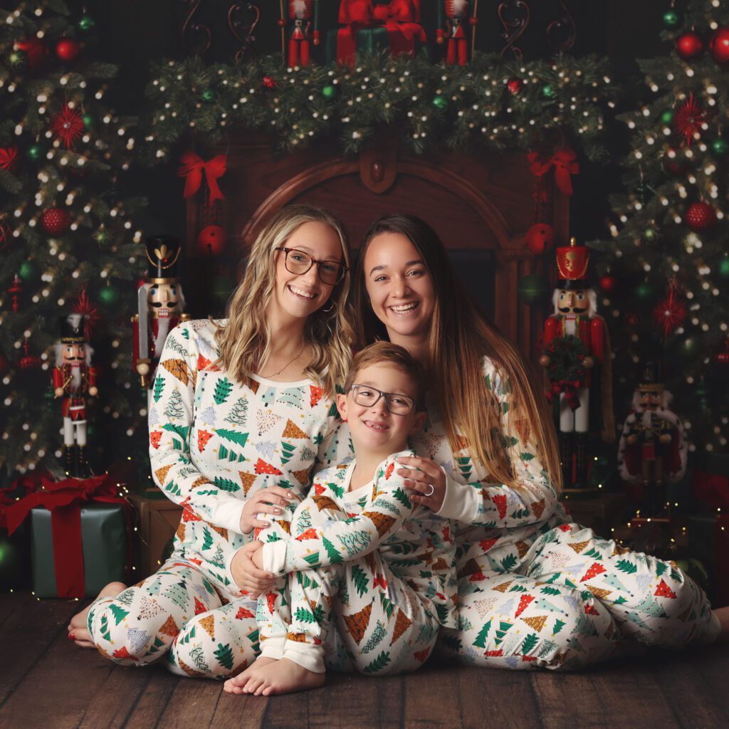 two teenage sister sitting with younger frother in front of a Christmas fireplace