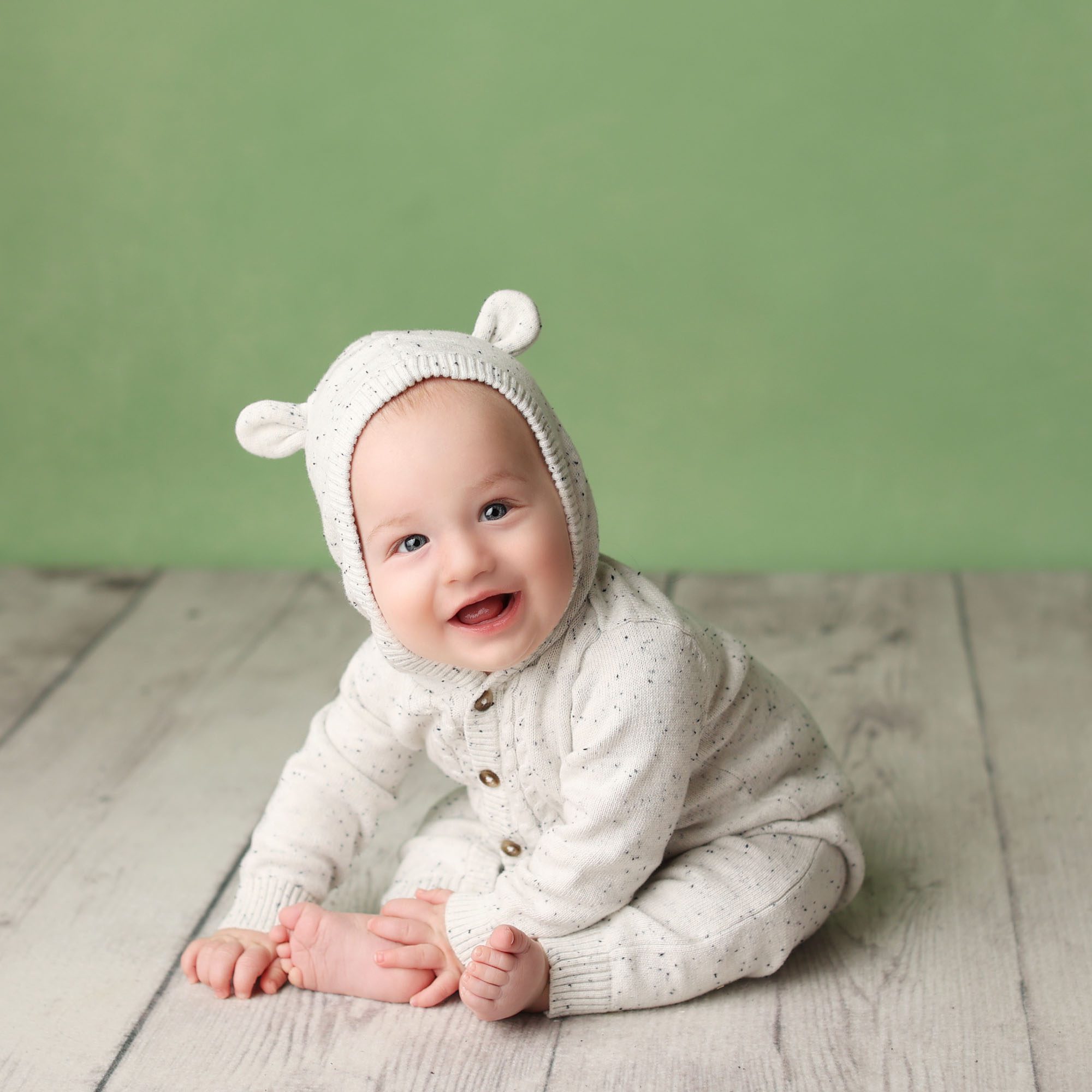 Liberty, MO baby boy sitter session in white bear ear hood romper on wood floor with green backdrop