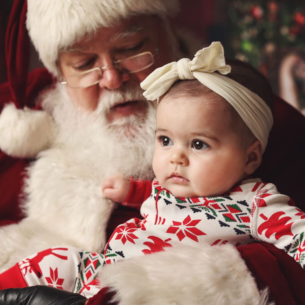 Baby girl looking ahead while Santa looks down at her during Christmas photos