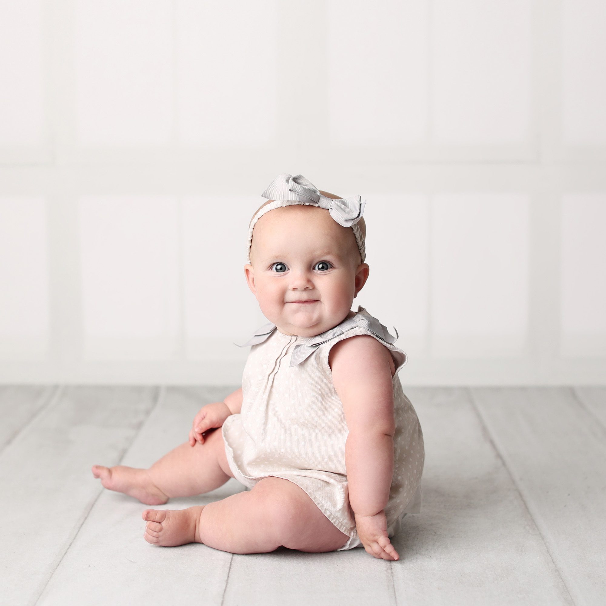 Lee's Summit, MO baby girl sitter session in white and gray neutral studio smiling on white floor