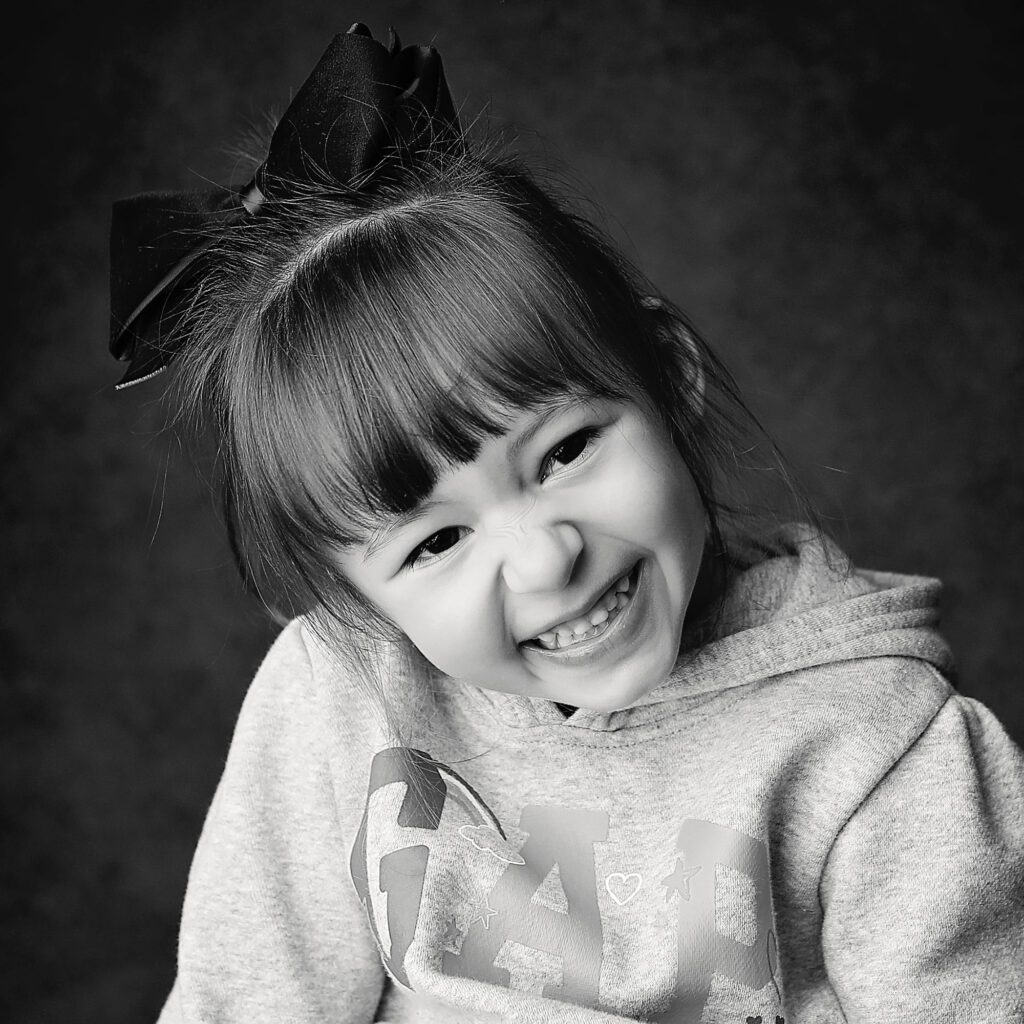 Black and white close up studio portrait of a little girl laughing with a bow in her hair