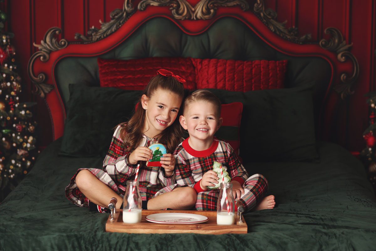 Brother and sister snuggled together holding Christmas cookies on a holiday bed