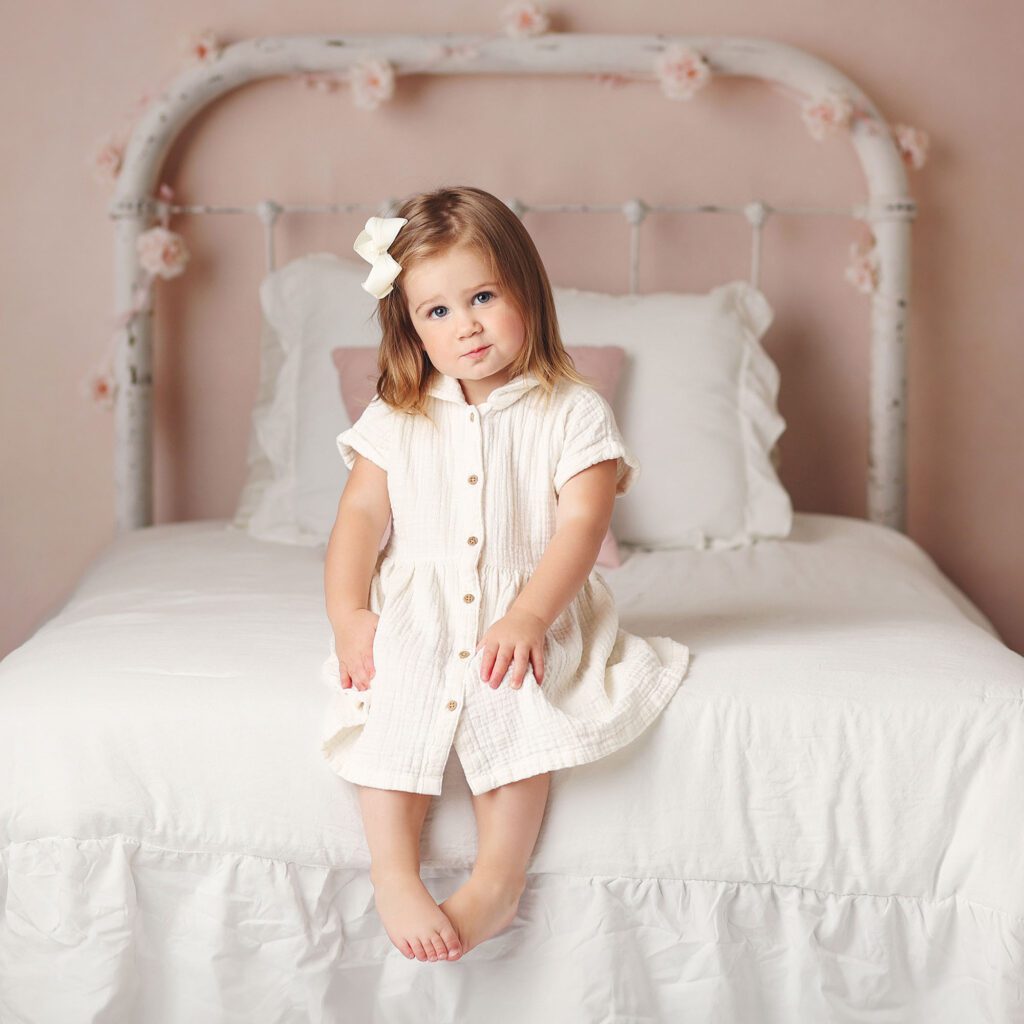 Child studio portrait of little girl sitting on the edge of a bed in a studio portrait