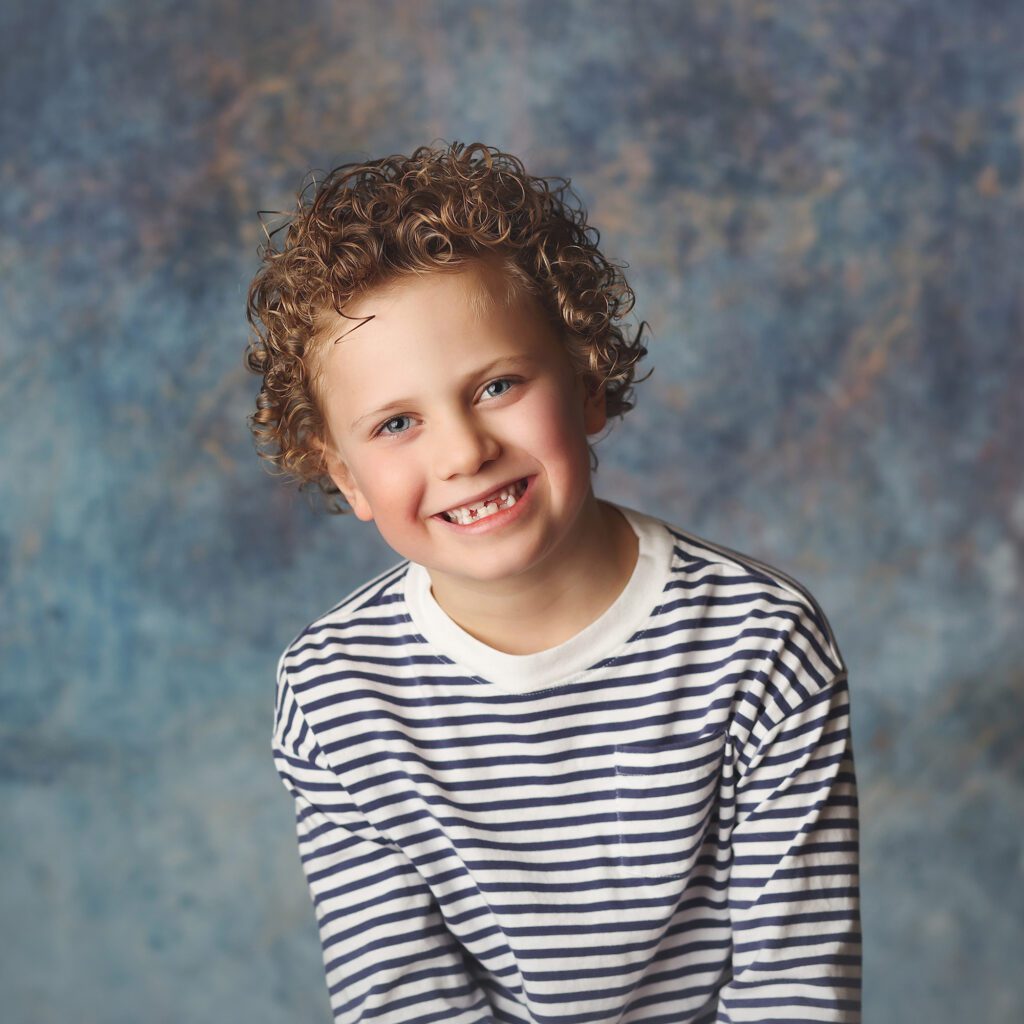 Little boy smiling in a studio portrait with a blue marbled backdrop