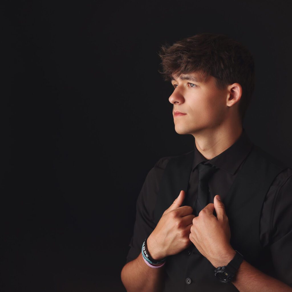 Profile studio portrait of a teenage boy dressed in black against a dark background