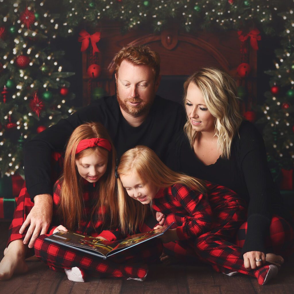 Paretns reading a Christmas book with their two daughters in matching pajamas