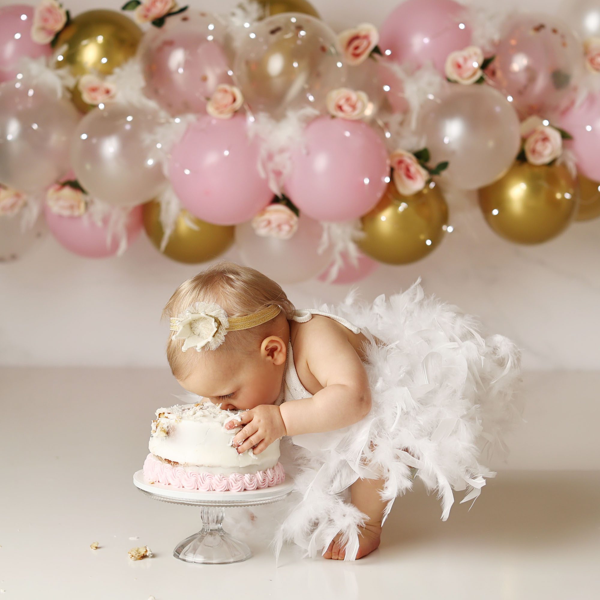 Overland Park, KS Swan Lake cake smash girl in feather skirt smashing cake with balloon garland backdrop